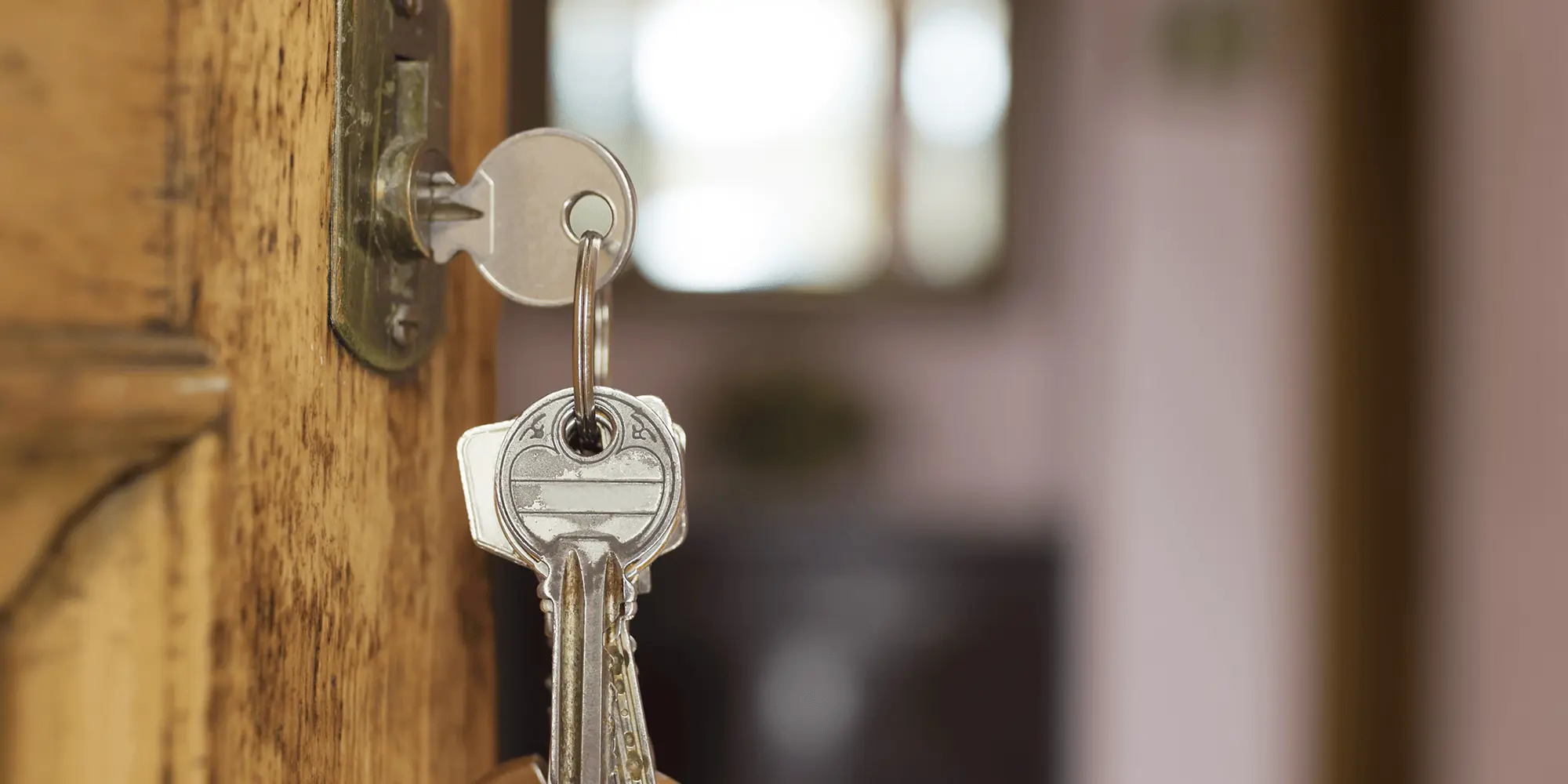 Close-up of silver keys in a brass door lock by Commercial Locksmith Las Vegas with blurred open doorway.